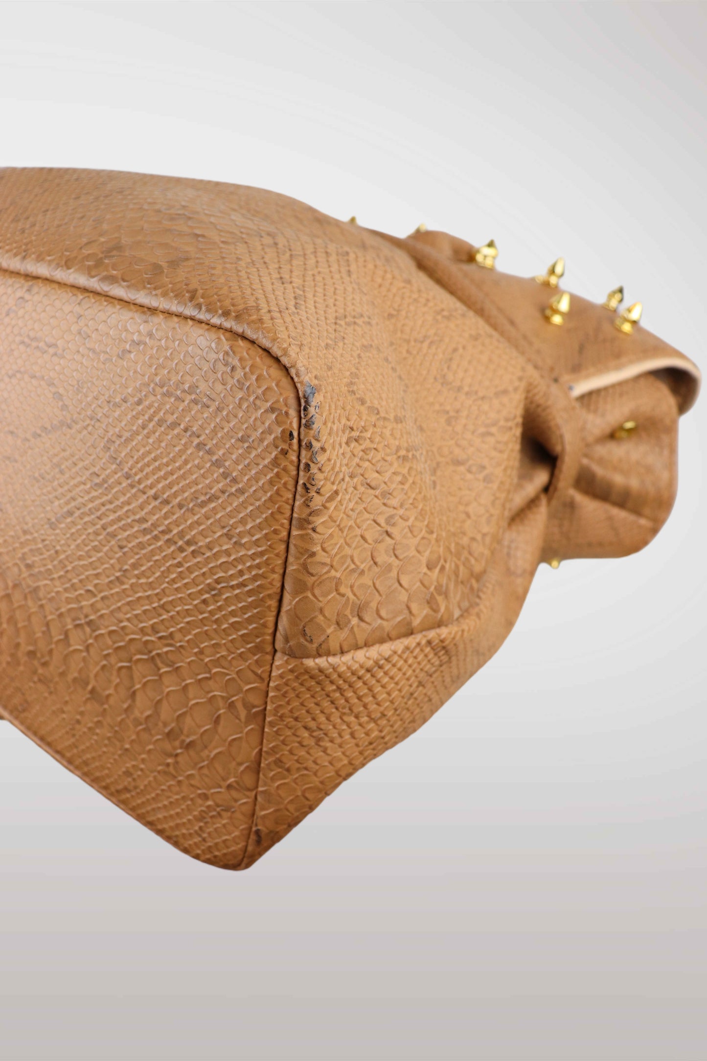 Brown textured handbag with gold studs on a light gray background