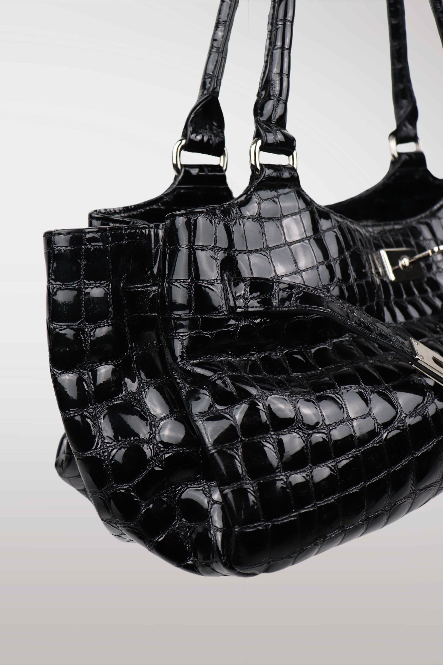Three black crocodile-patterned handbags stacked on a light gray background