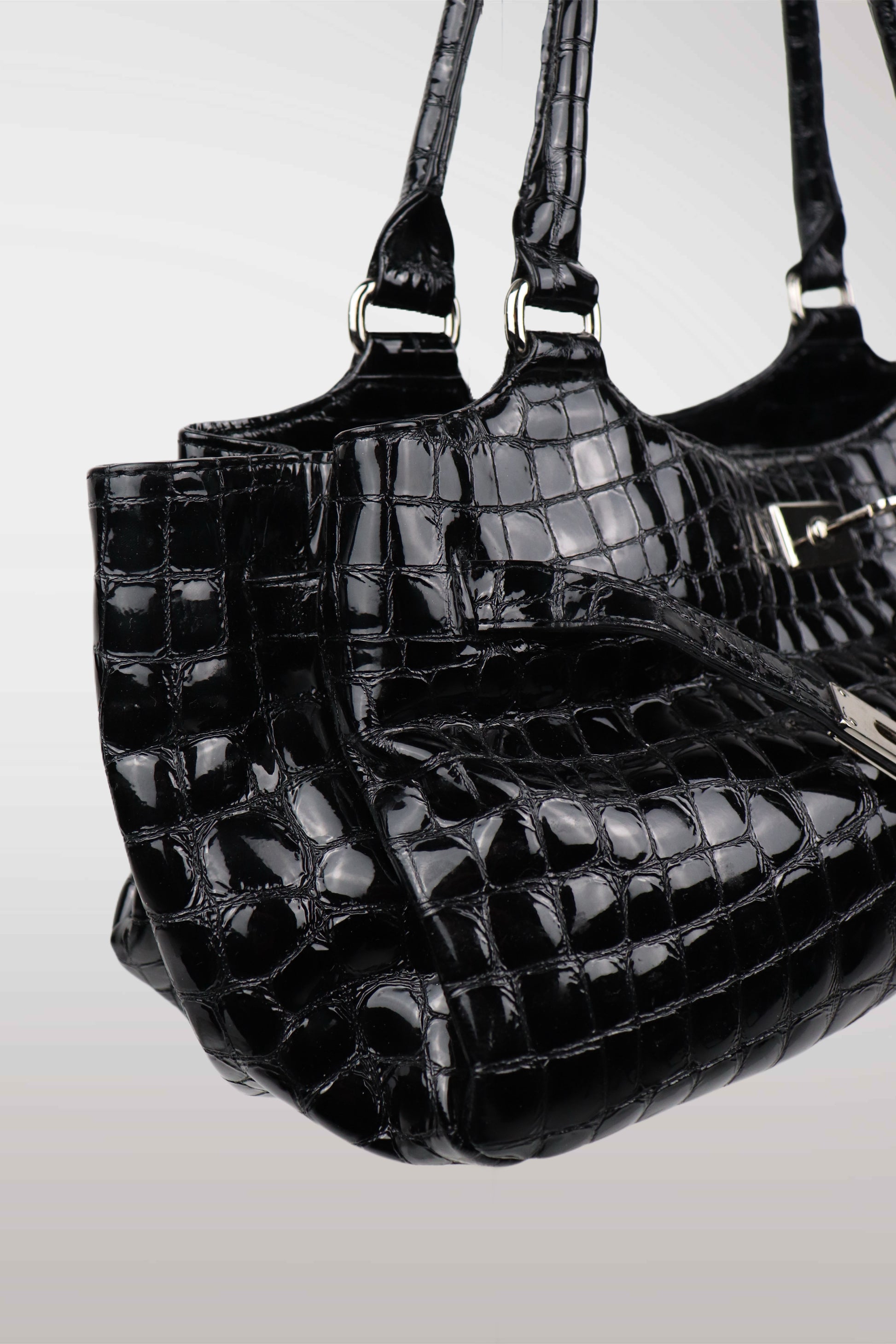 Three black crocodile-patterned handbags stacked on a light gray background