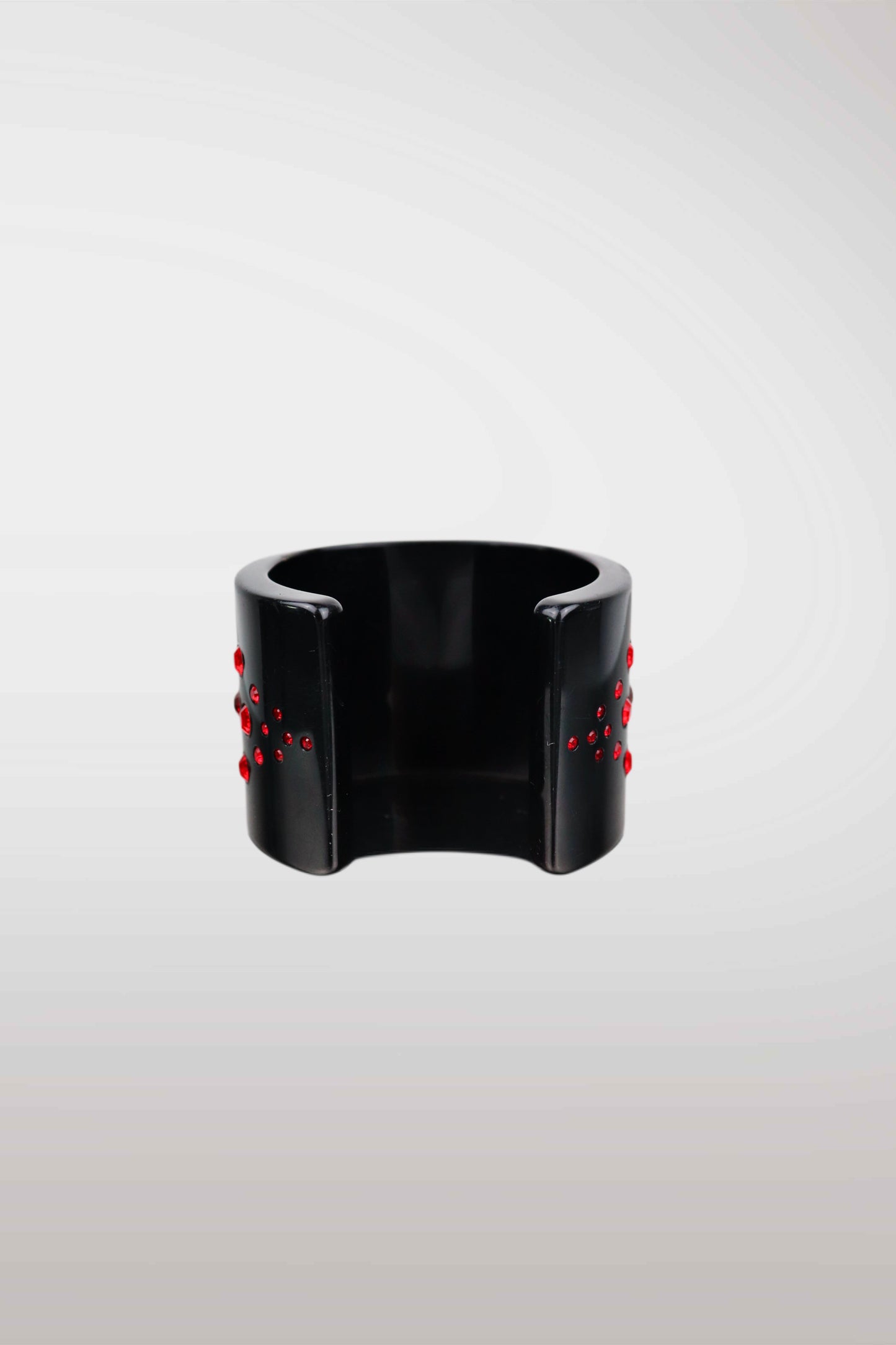 A wide black cuff bracelet with small red bead-like accents on both sides, photographed against a light gray gradient background.