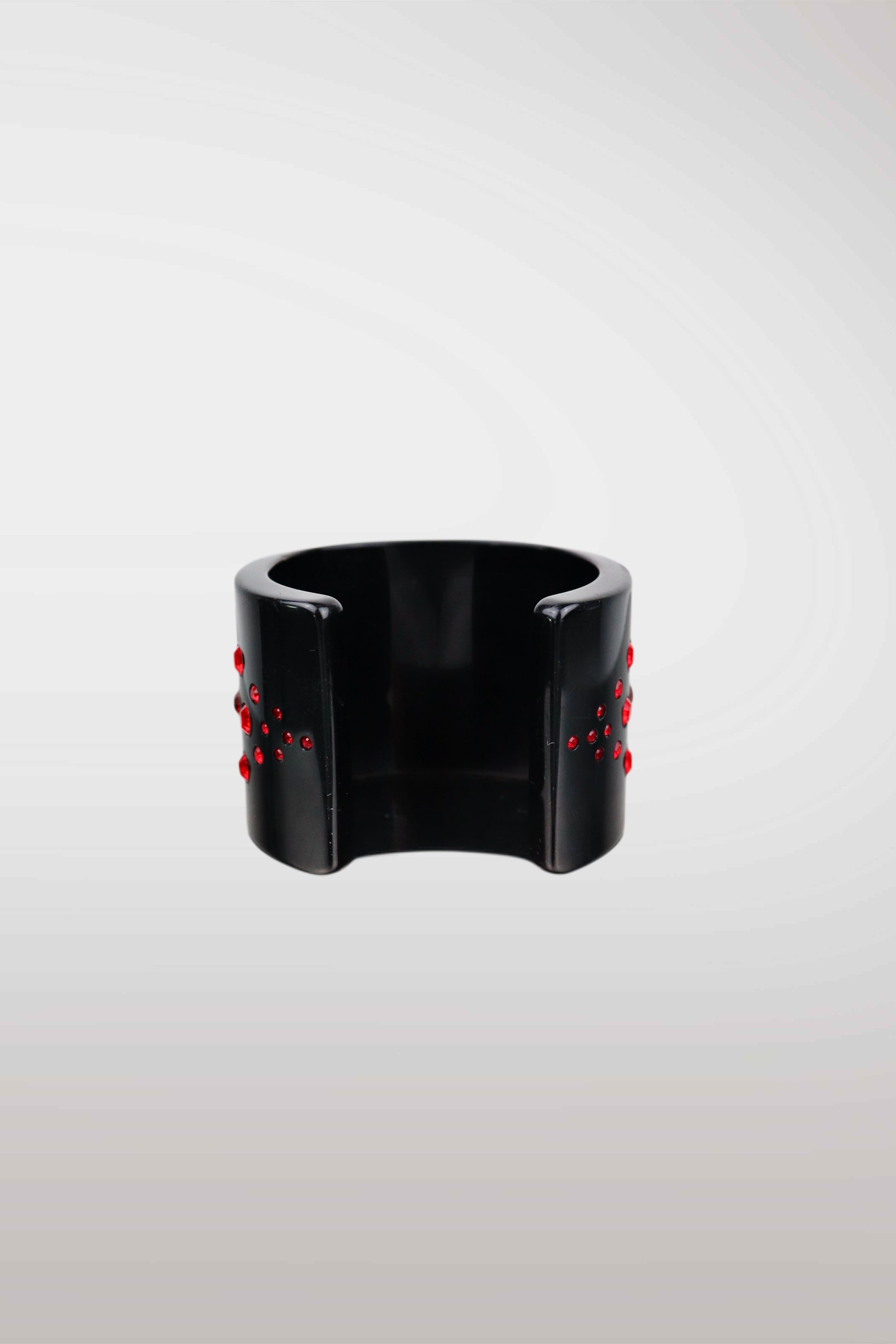 A wide black cuff bracelet with small red bead-like accents on both sides, photographed against a light gray gradient background.