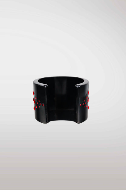 A wide black cuff bracelet with small red bead-like accents on both sides, photographed against a light gray gradient background.