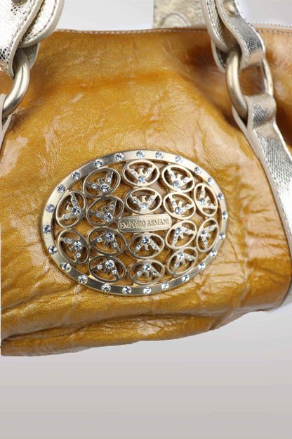 Close-up of a brown leather handbag with a decorative metal emblem on a white background