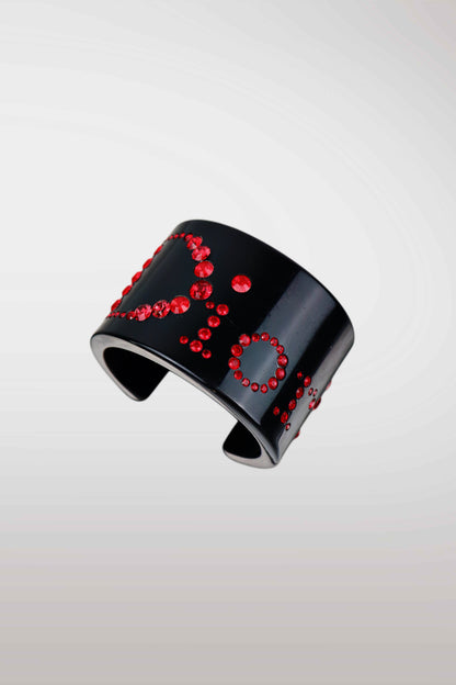 A glossy black cuff bracelet decorated with sparkling red rhinestones arranged in abstract circular patterns, shown against a light gray gradient background.
