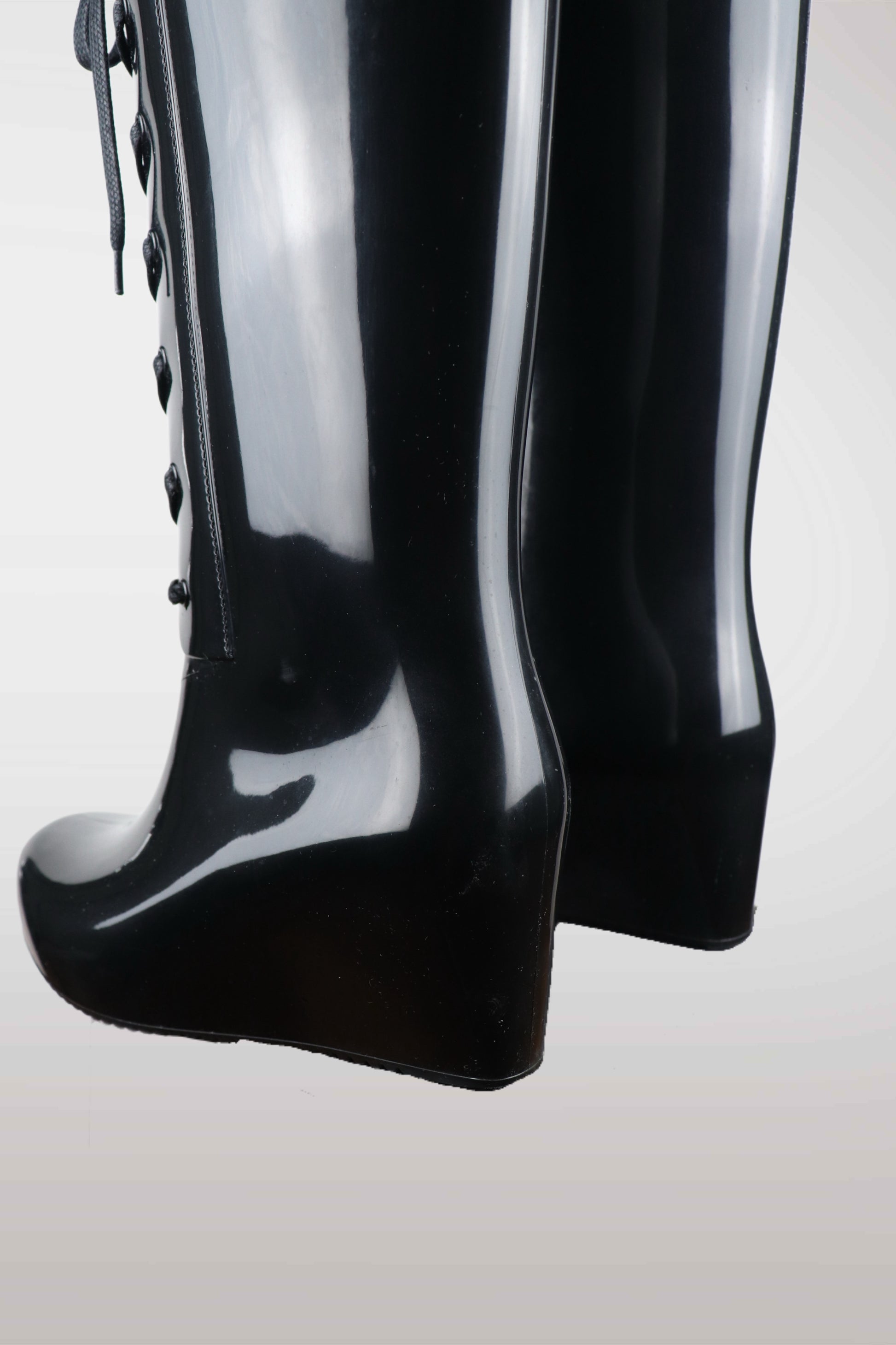 Yves Saint Laurent women’s black wedge rain boots with lace-up front design, glossy waterproof rubber finish, mid-calf height, and hidden platform heel — luxury designer rain footwear combining elegance and practicality, perfect for chic all-weather style