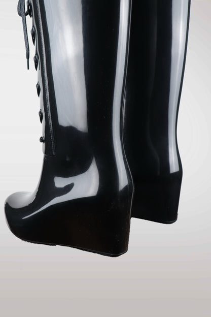 Yves Saint Laurent women’s black wedge rain boots with lace-up front design, glossy waterproof rubber finish, mid-calf height, and hidden platform heel — luxury designer rain footwear combining elegance and practicality, perfect for chic all-weather style